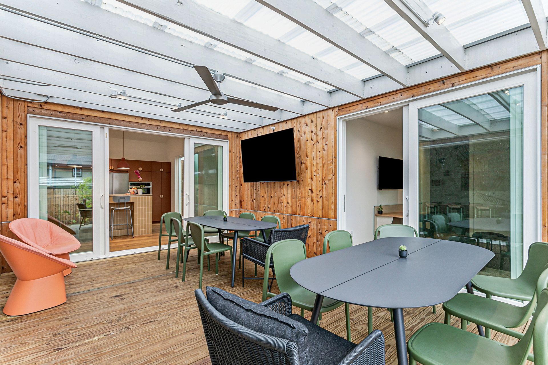 Outdoor dining area with tables, green chairs, and a mounted TV on a wooden wall.