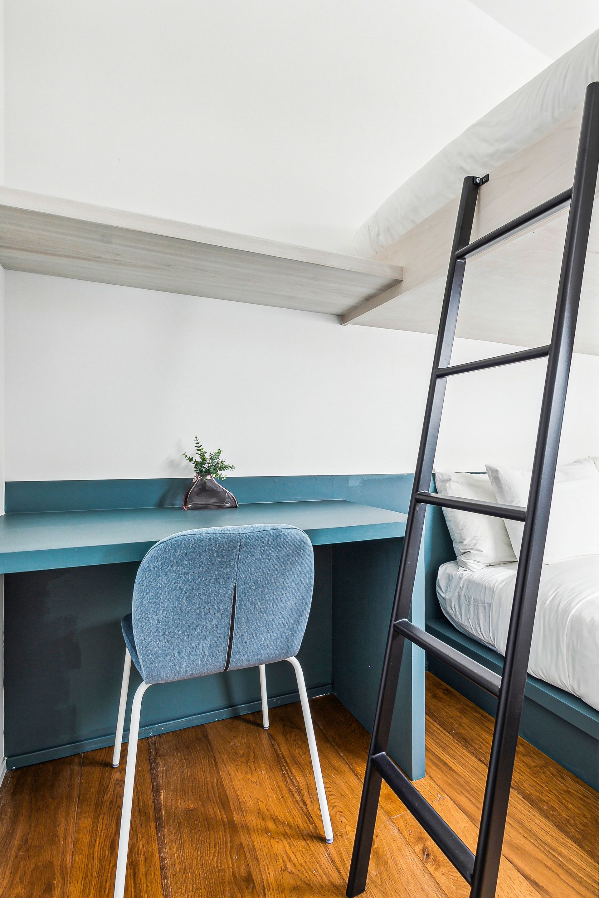Desk and chair in teal by a bed, wooden floor, and a black ladder.