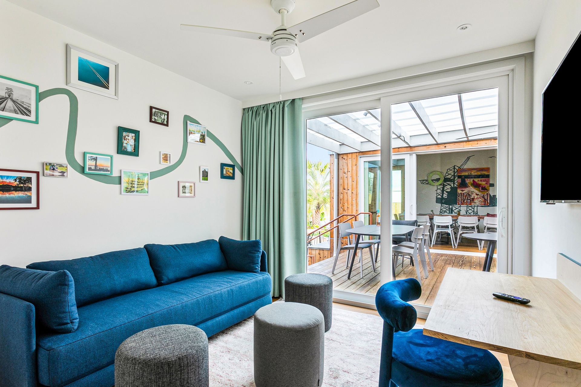 A bright living room with a blue sofa, decor on the wall, and an open door to an outdoor dining area.