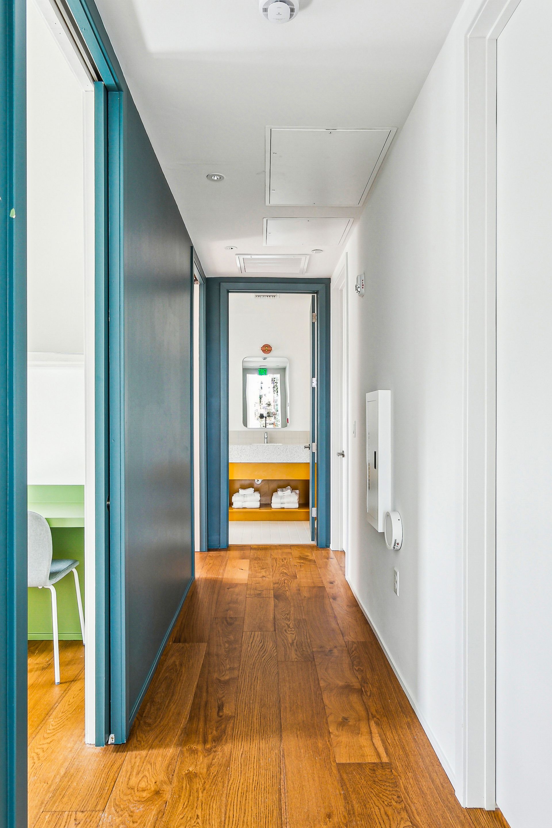Narrow hallway with wood floor, leading to a bathroom. Teal sliding door on the left.