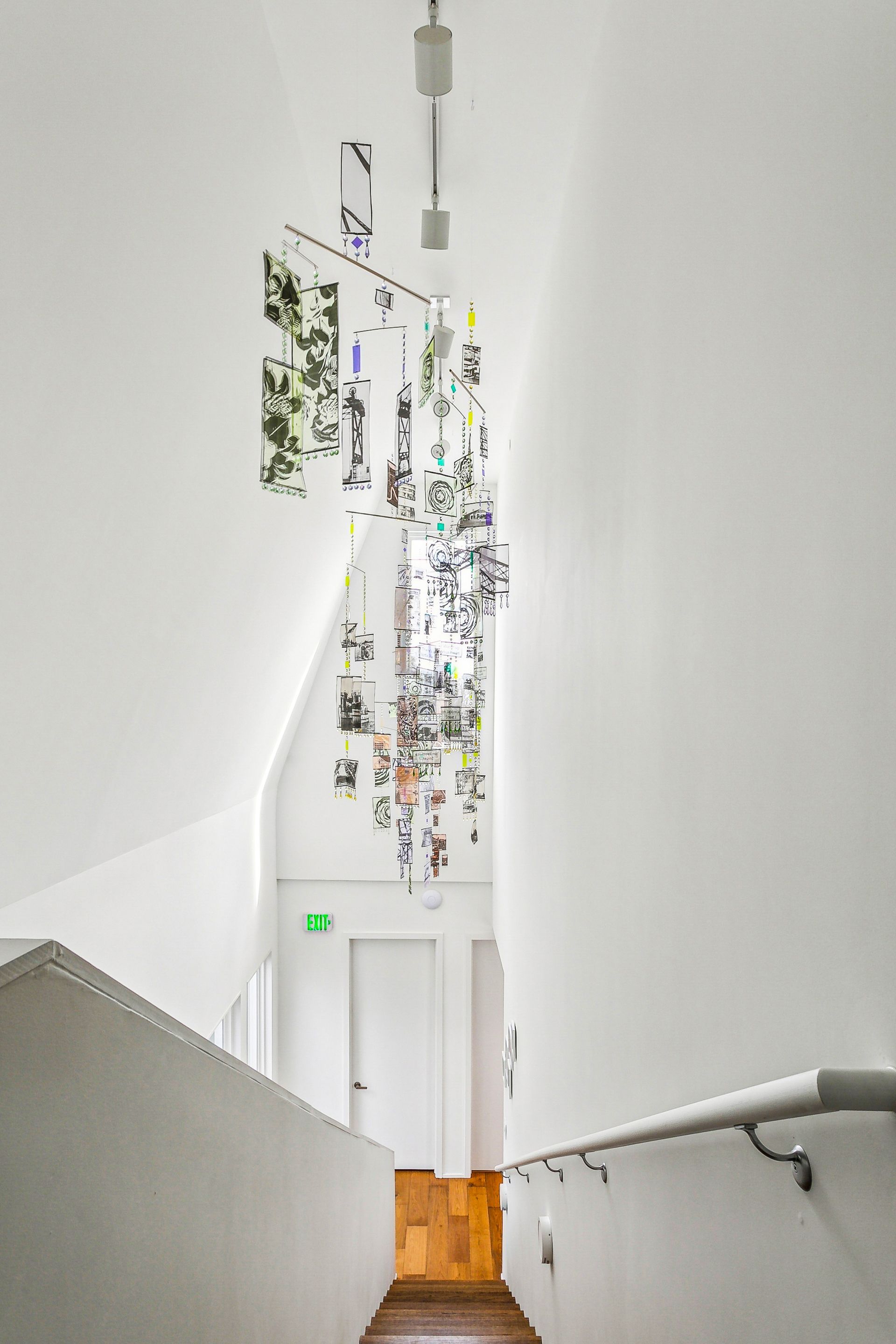 A bright white stairwell with a hanging mobile of photos and a handrail.