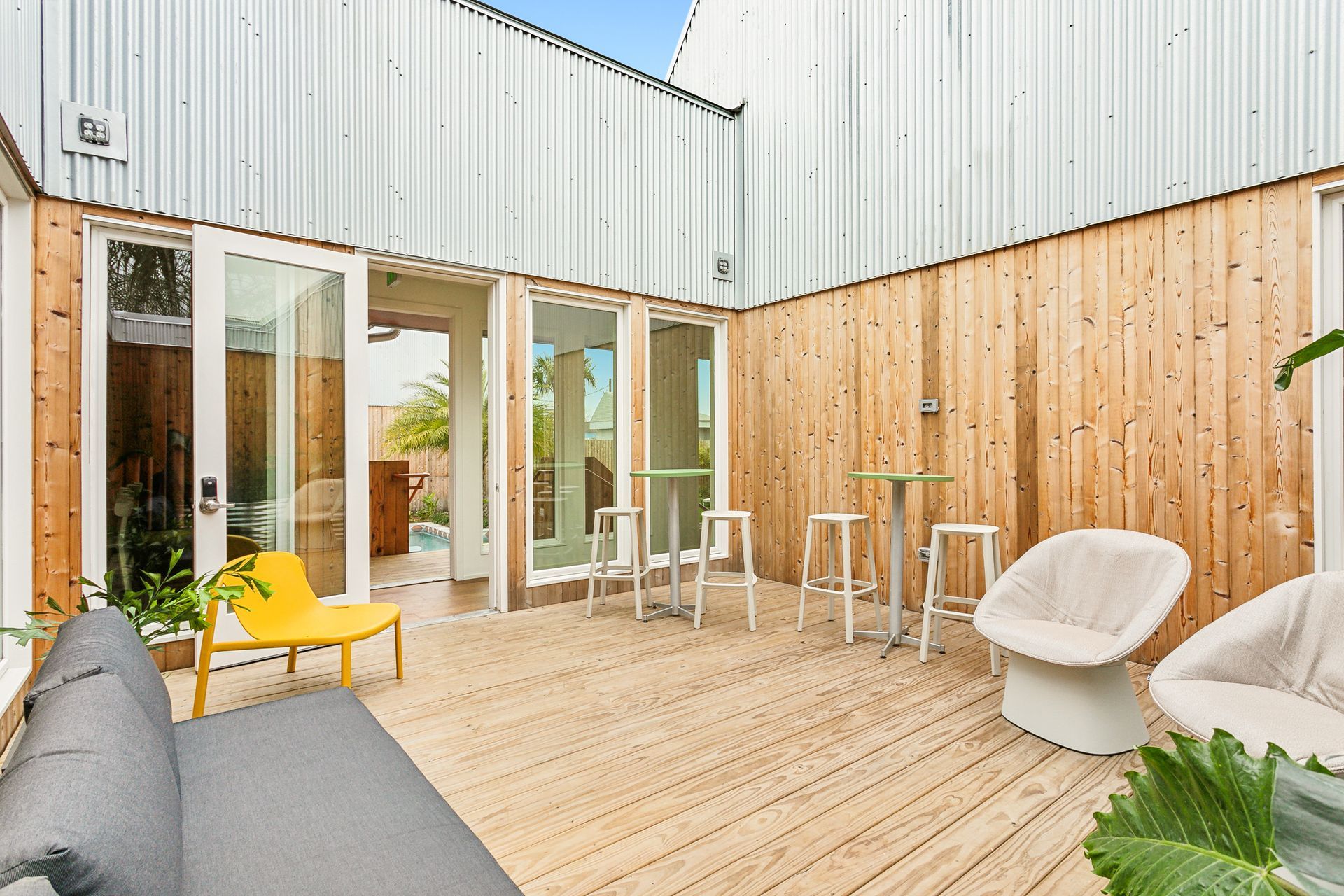 Outdoor patio with wooden deck, light wood and corrugated metal walls, various white and yellow seating.