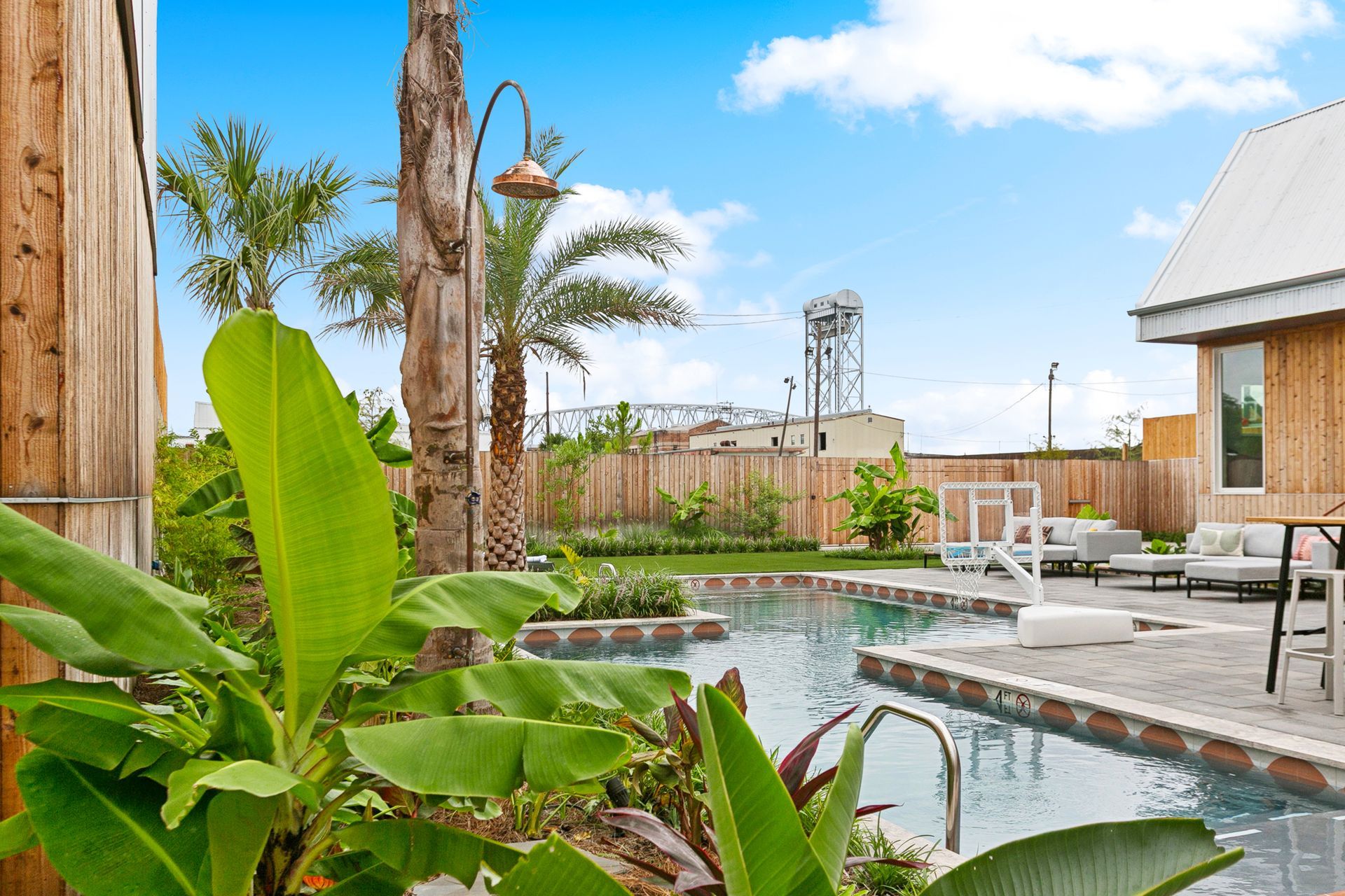 Tropical pool scene with palm trees, lounge chairs, and a bridge in the background.