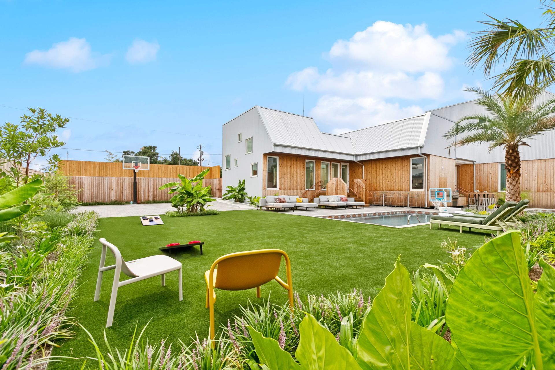 Lush backyard with modern home, green lawn, pool, and chairs under a blue sky.