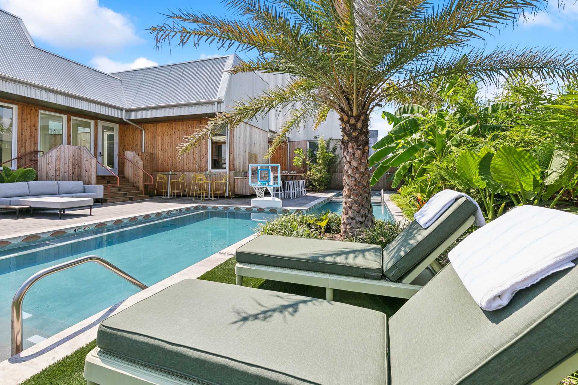 Poolside scene with lounge chairs, palm tree, and buildings.