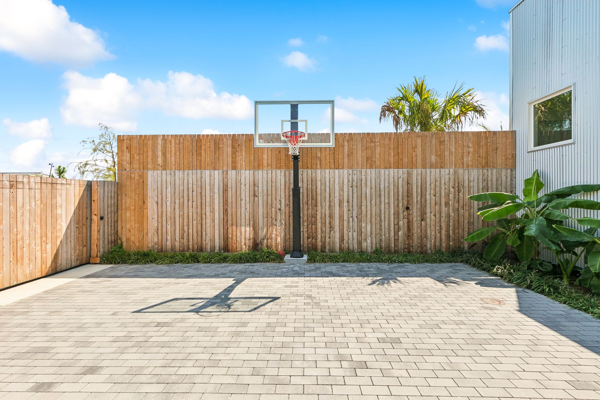 Basketball hoop on a brick patio against a wooden fence under a blue sky.