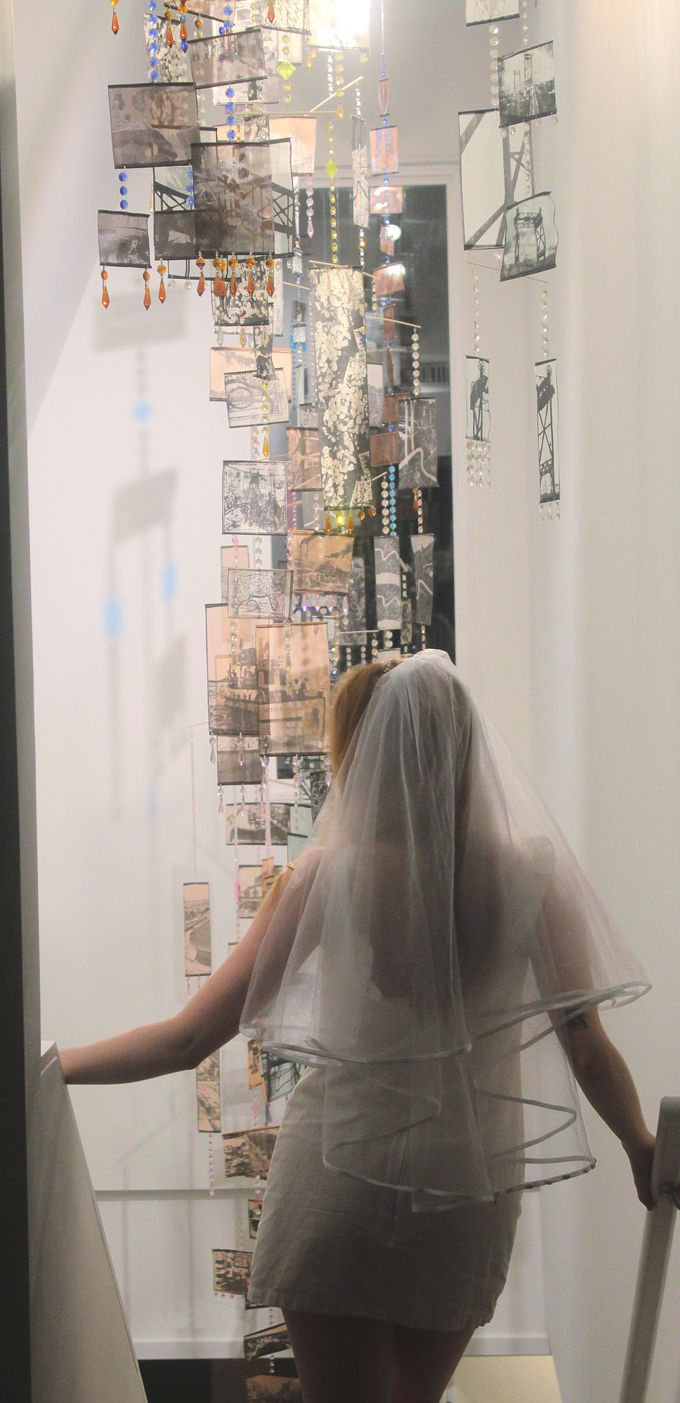 Woman in bridal veil walks up stairs, art installation on wall.