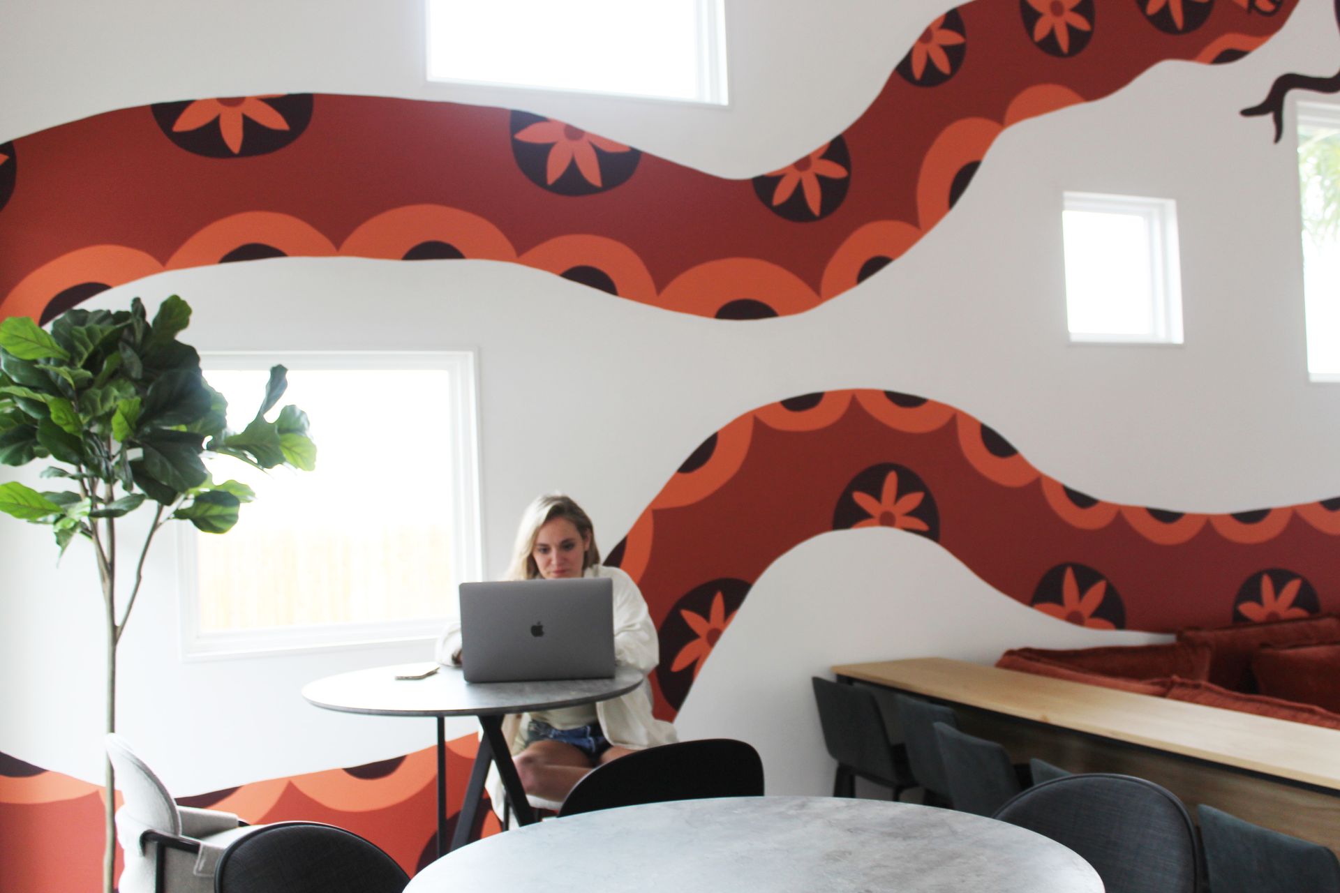 Woman working on laptop in bright room with decorative wall art.