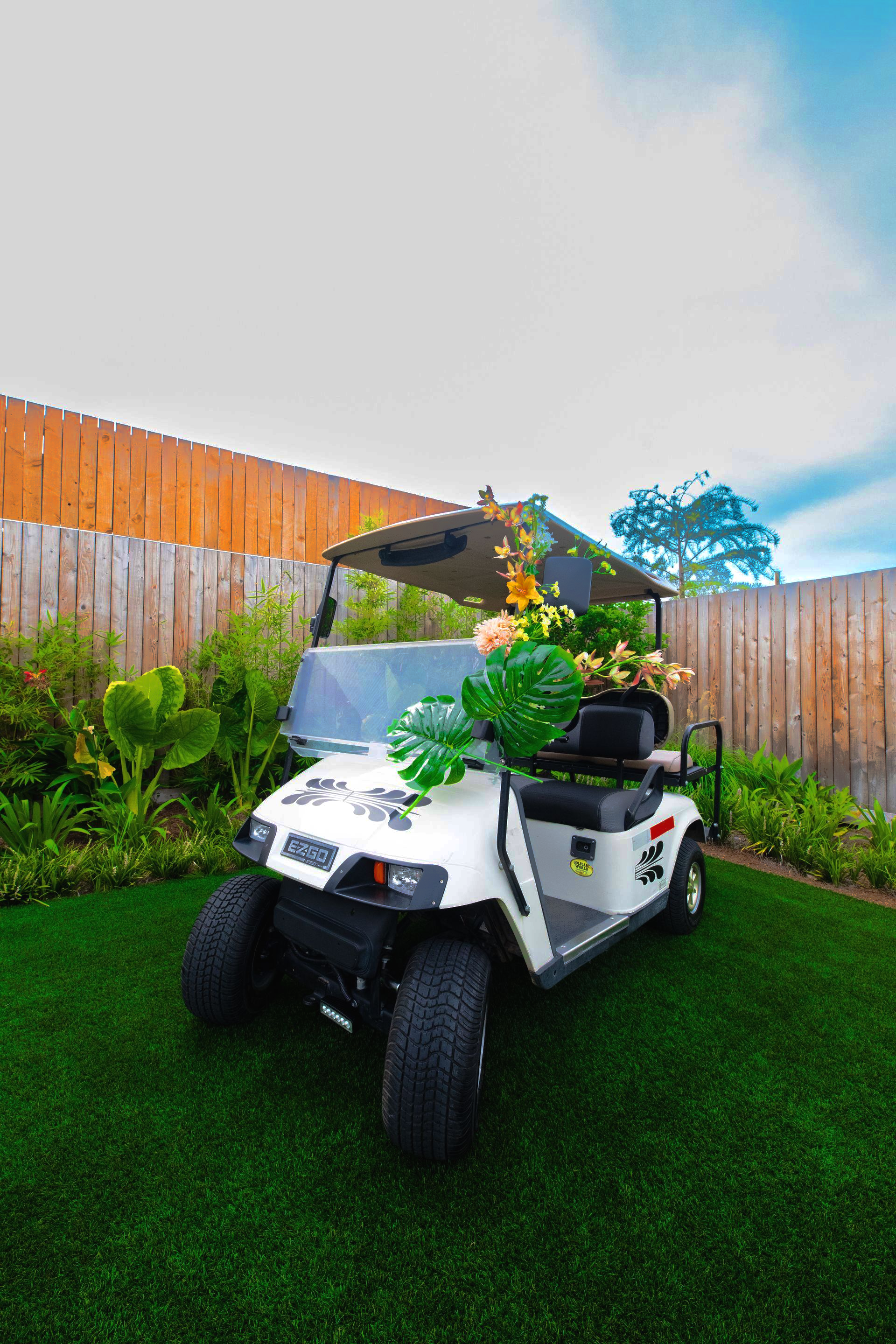 White golf cart decorated with flowers parked on green turf, in a backyard.