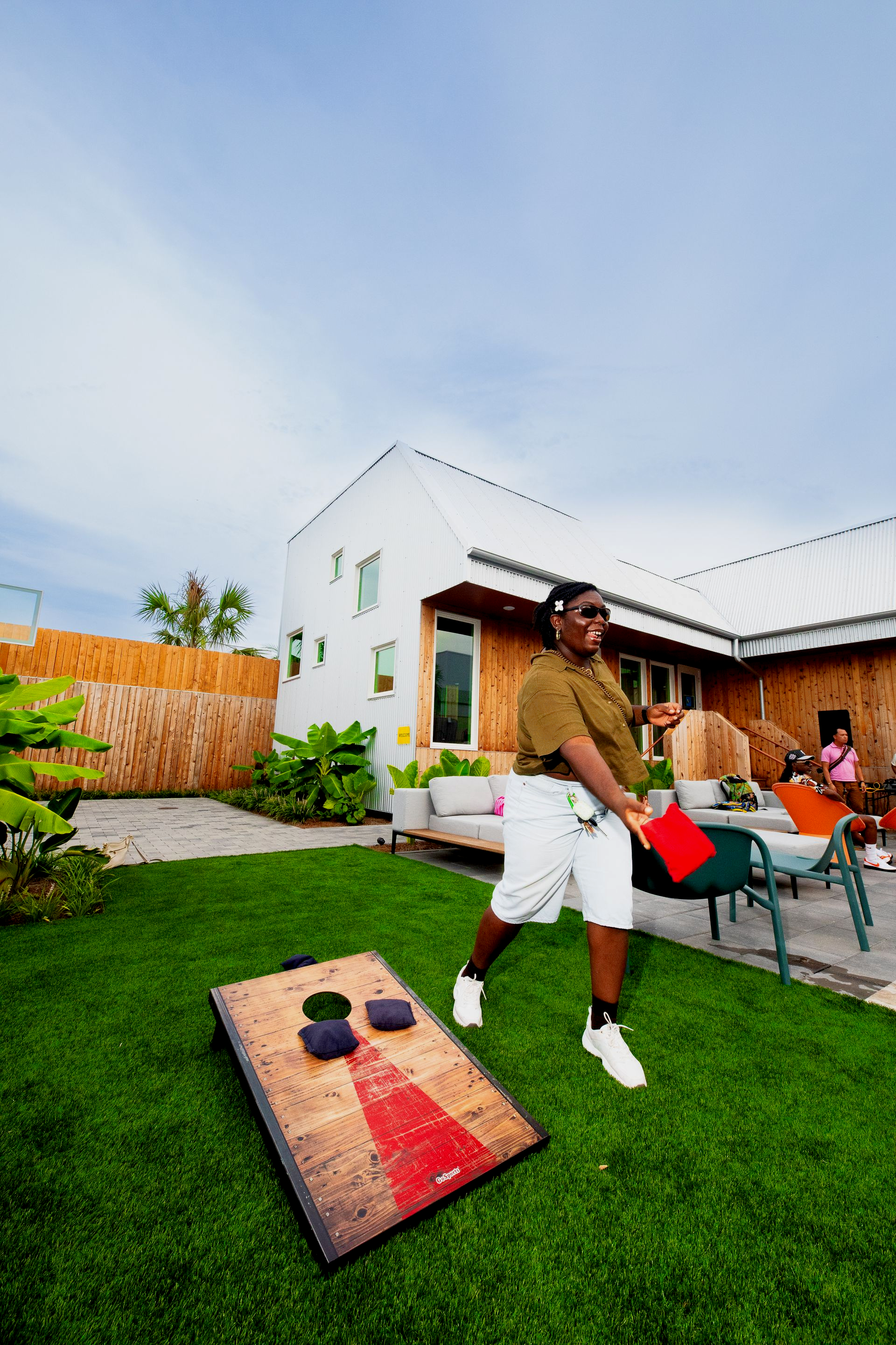 Man tossing a beanbag at a cornhole board on a green lawn, sunny day.