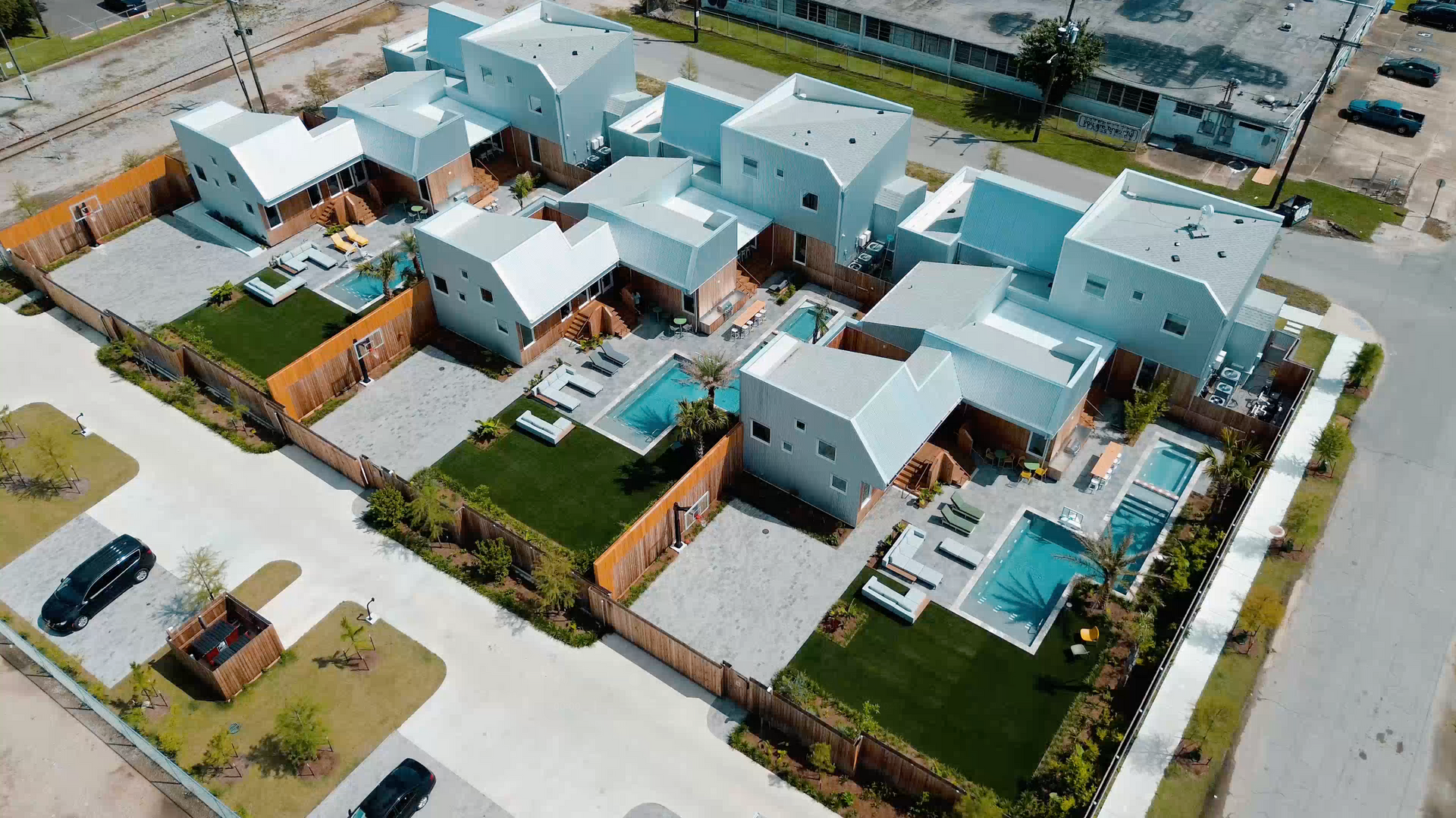 Aerial view of a modern residential neighborhood with white houses, turquoise pools, and green lawns.