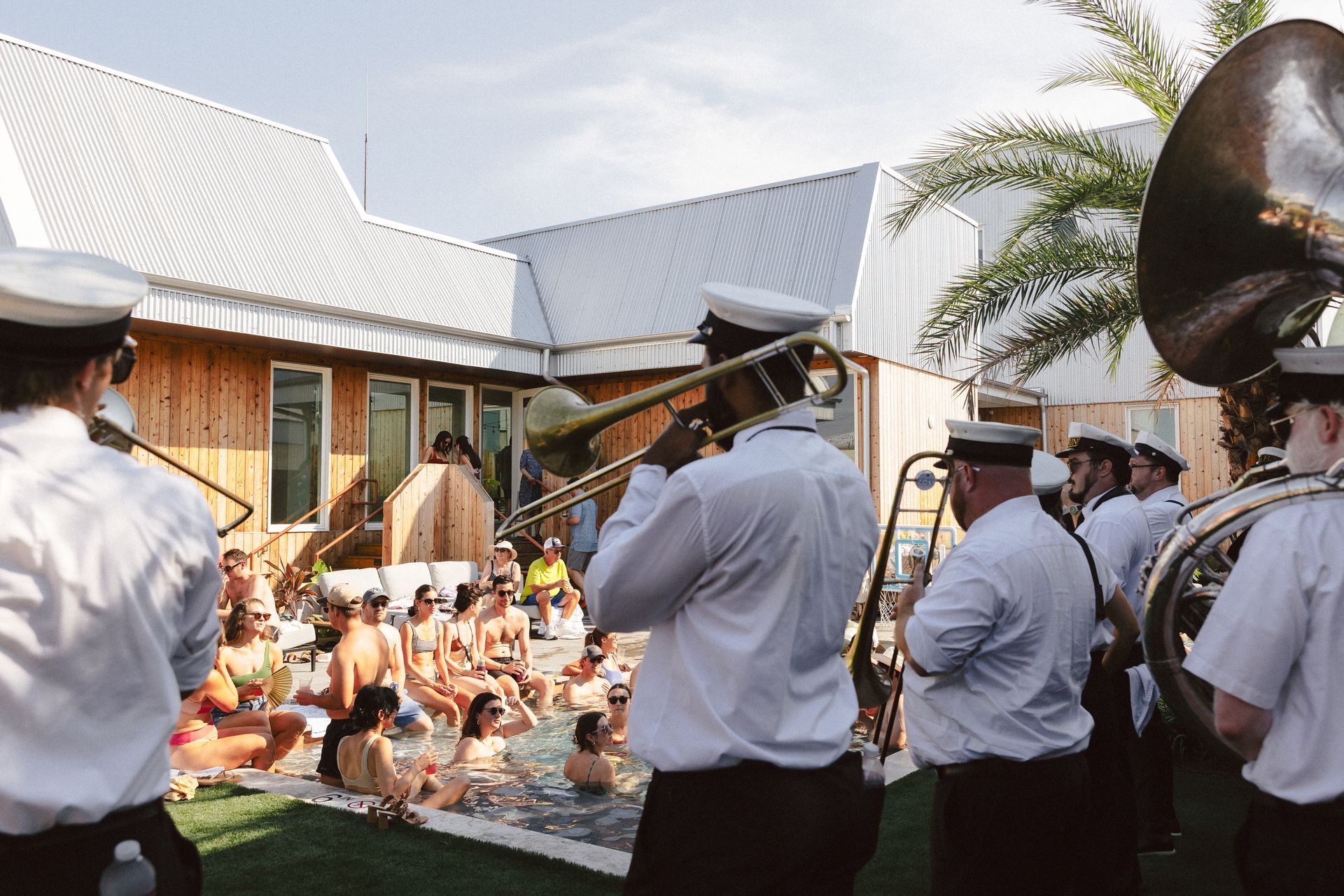 A brass band performs poolside for people enjoying the water, in a modern outdoor setting.