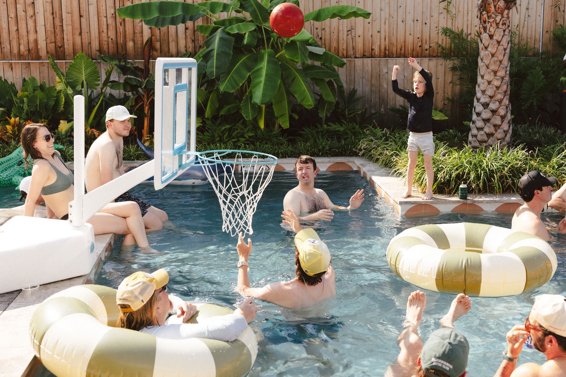 Man throwing a bean bag at a cornhole board on a grassy lawn. White house in the background.