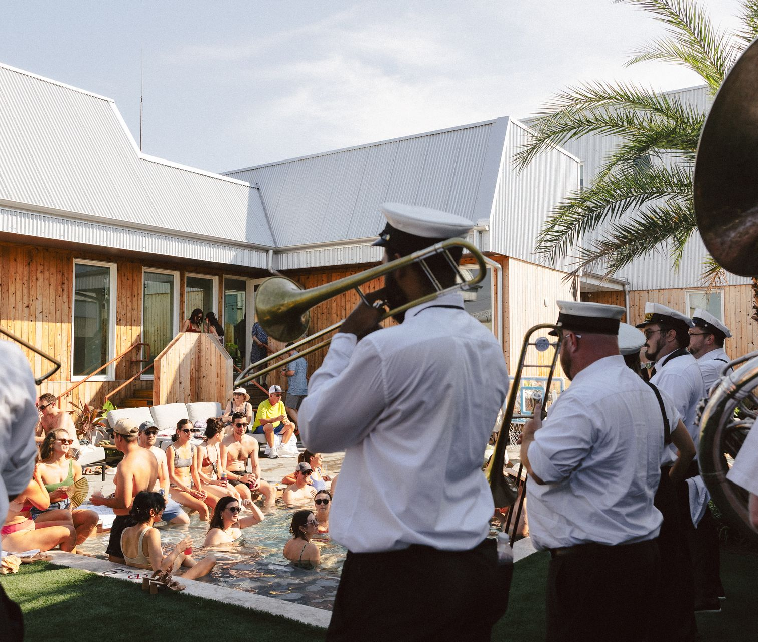 Band playing brass instruments beside a pool at an outdoor gathering under a sunny roofline