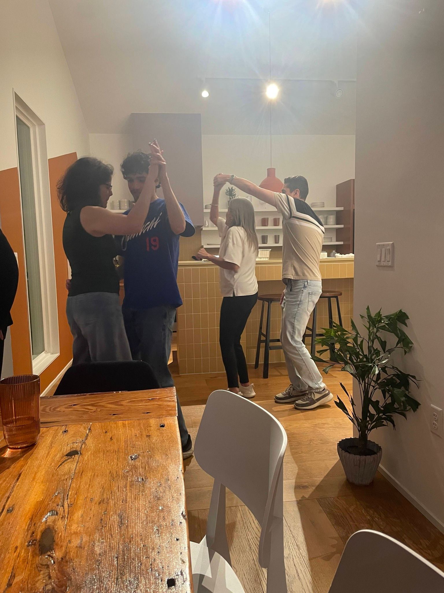 People dancing and clapping in a living room with warm lighting and a wooden table in the foreground