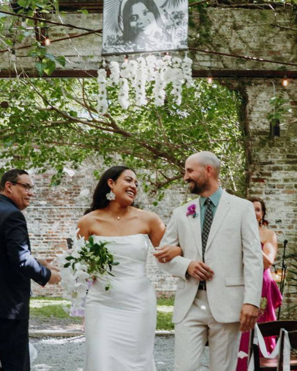 Bride and groom smiling and walking outdoors beneath ivy and stone archway
