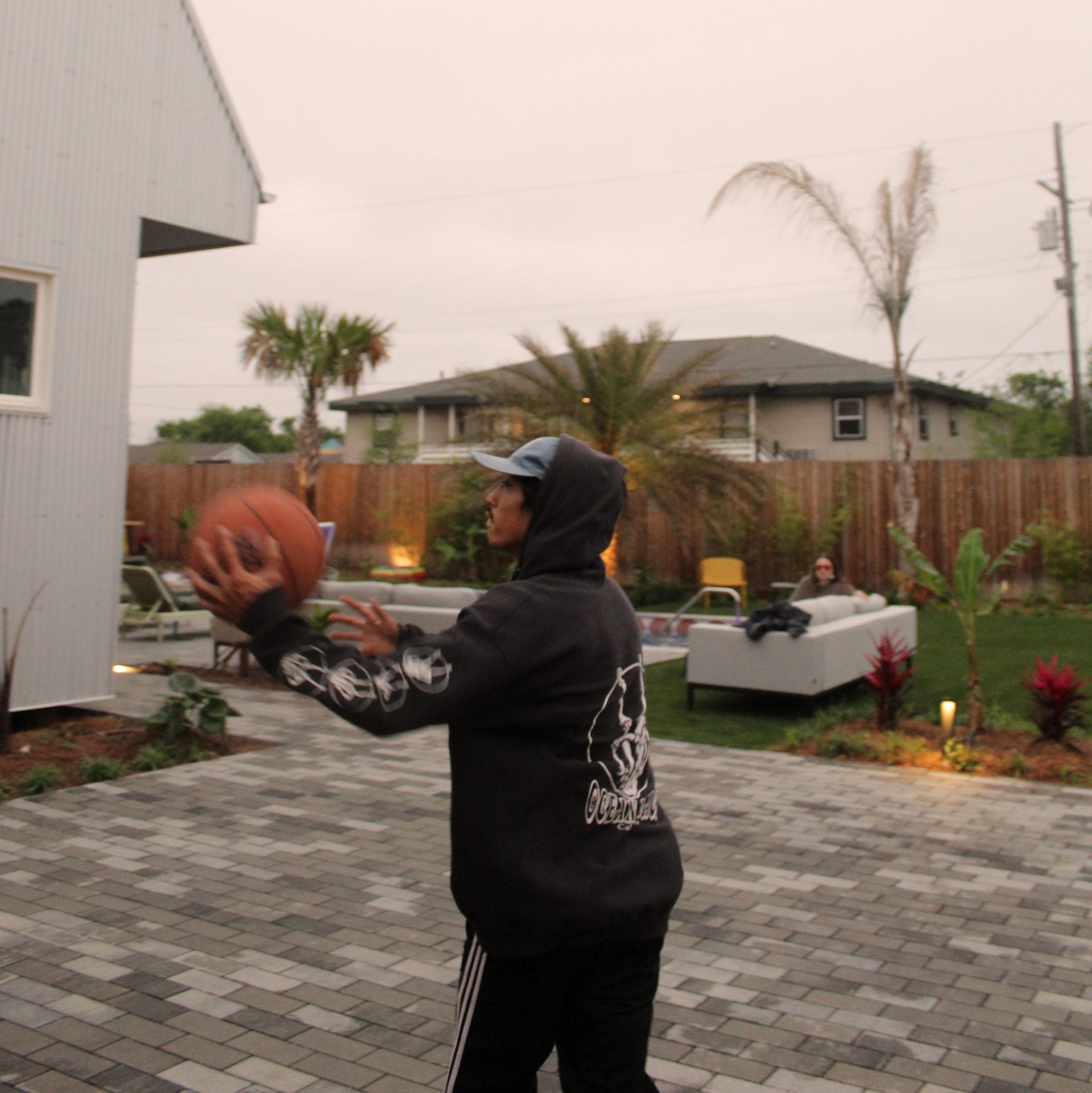 Person in hoodie throwing basketball outdoors on a patio.