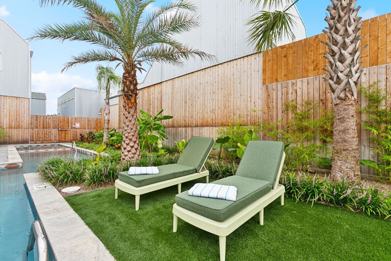 Two green chaise lounges beside a pool with a palm tree in a backyard setting.