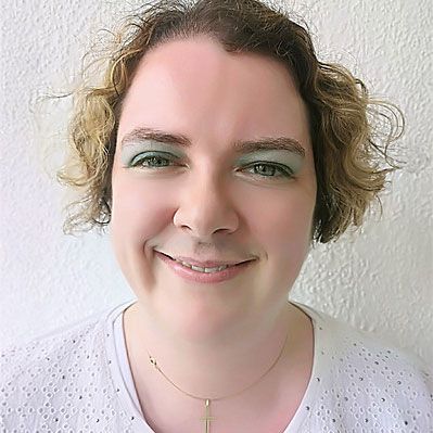 Frau Pahl mit lockigem blondem Haar und grünem Lidschatten, lächelnd.