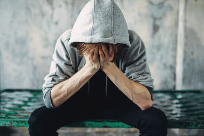 Person in einem grauen Kapuzenpullover, den Kopf in den Händen, sitzt mit hängenden Schultern da, möglicherweise verzweifelt.