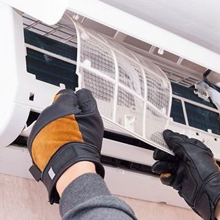 Una persona con guantes está limpiando un aire acondicionado.