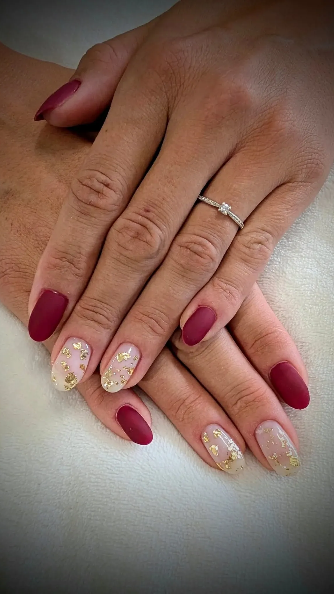 Des mains aux ongles bordeaux mats, deux ornés de feuilles d'or, et une bague en diamant.