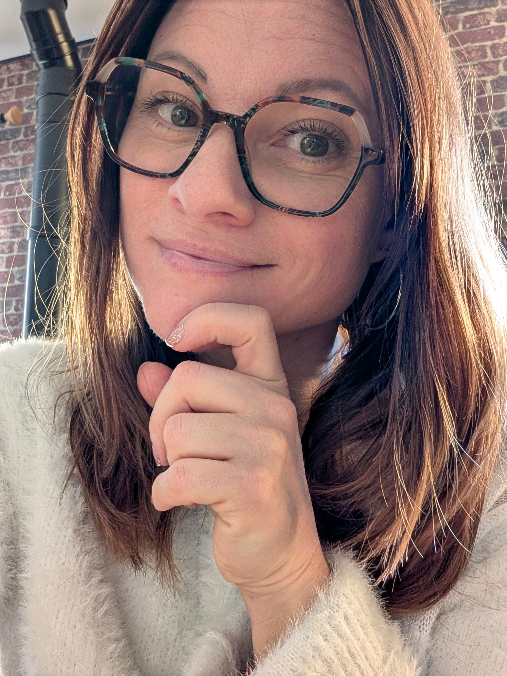 Femme portant des lunettes et un pull beige, debout dans une boutique avec des étagères remplies de bijoux et d'autres produits.