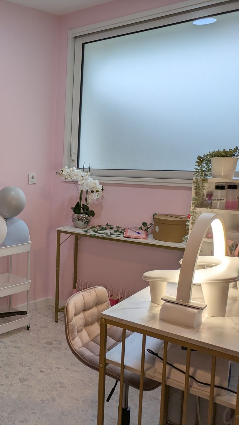 Intérieur rose d'un salon de manucure avec un poste de manucure, des étagères et une fenêtre.