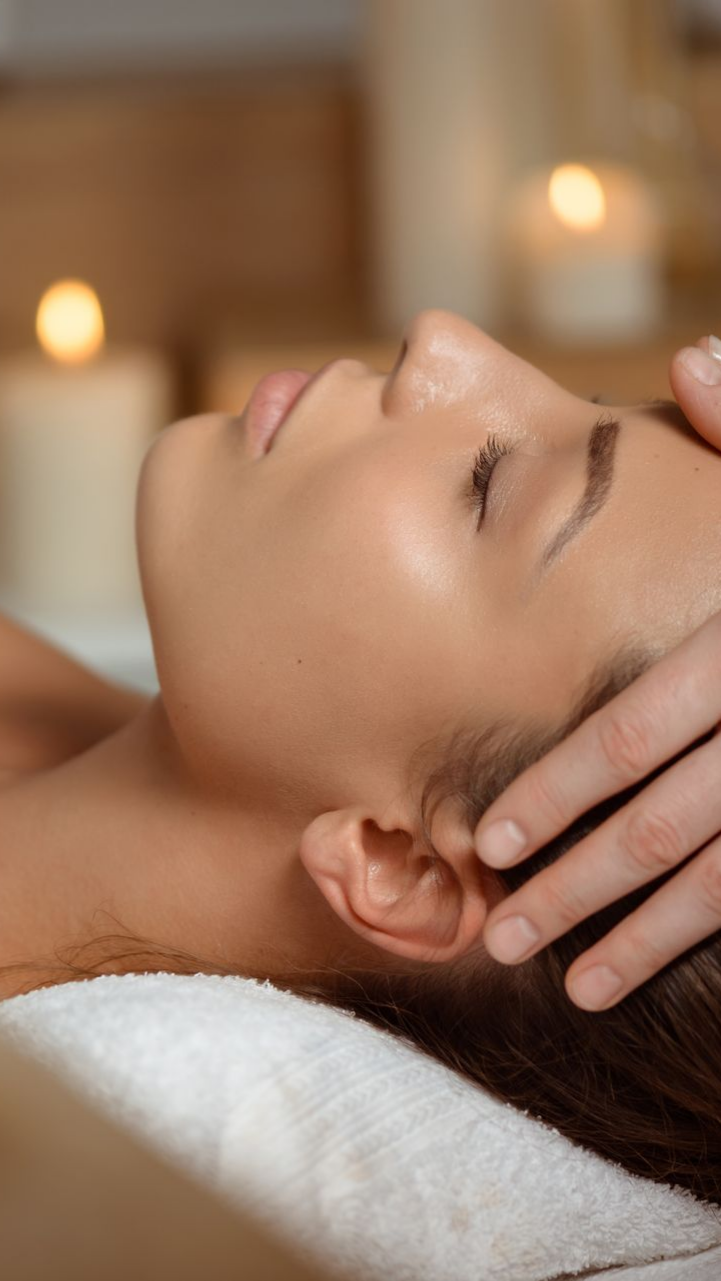 Une personne reçoit un massage de la tête, des bougies étant allumées en arrière-plan.