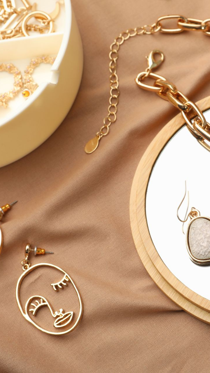 Des bijoux en or disposés sur un tissu beige, comprenant un collier, des boucles d'oreilles et une boîte à bijoux avec un miroir.