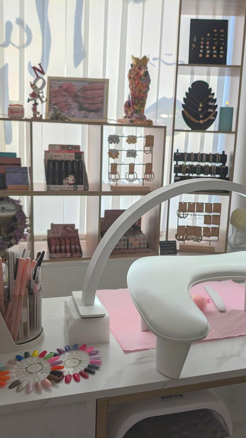 Espace de travail d'un salon de manucure avec des étagères de produits et un poste de travail éclairé, des échantillons de vernis à ongles sur la table.