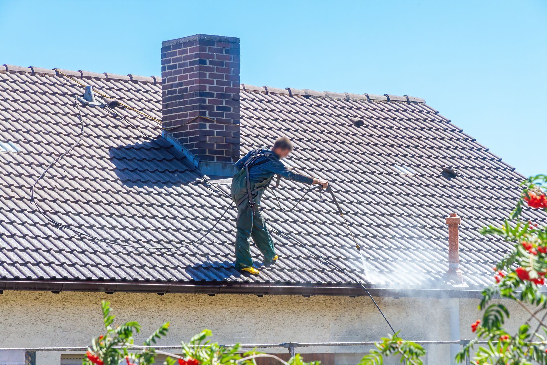 Un couvreur sur un toit en train de nettoyer la toiture avec un jet à haute pression