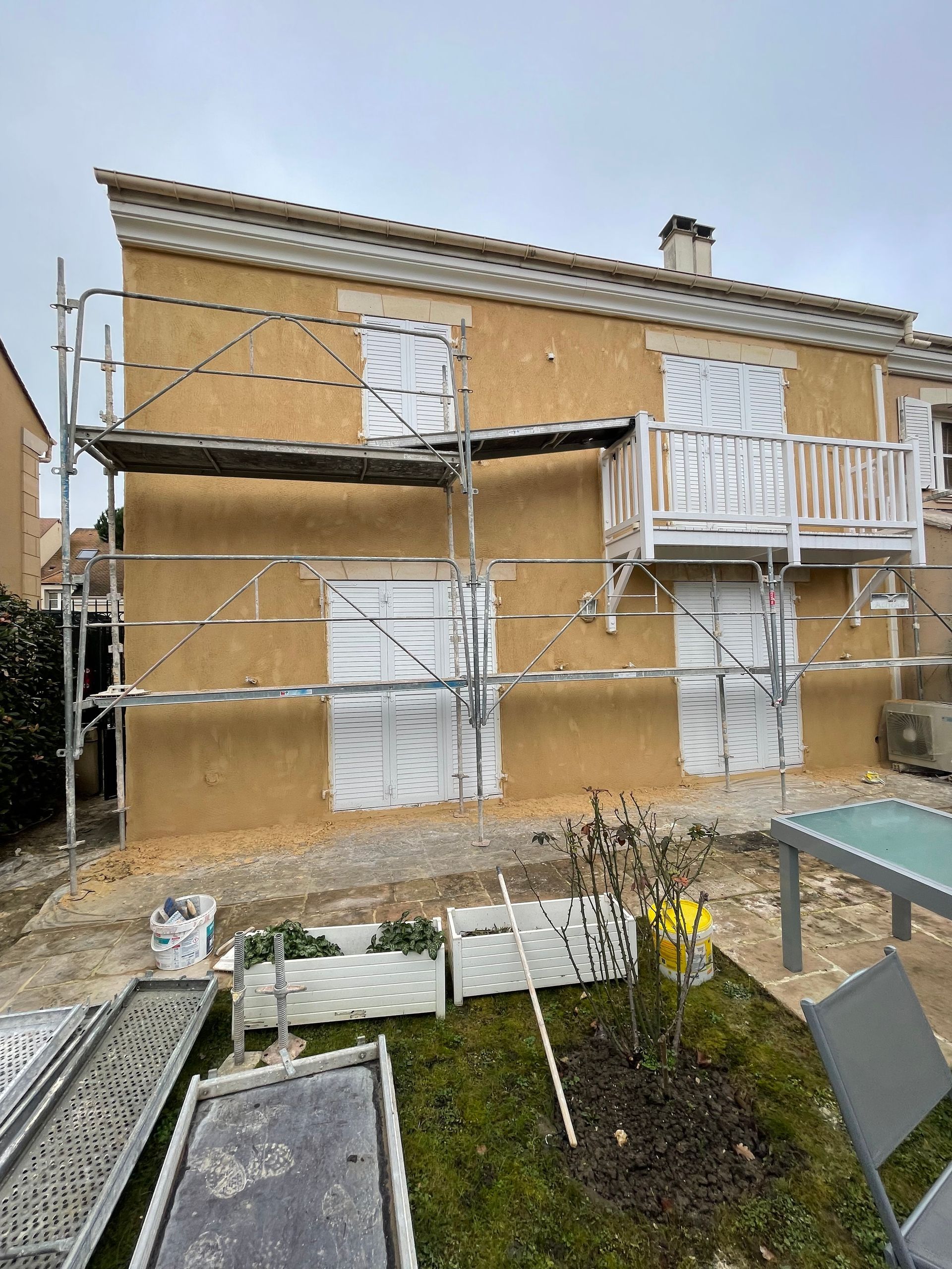 Un échafaudage devant une maison au crépi beige