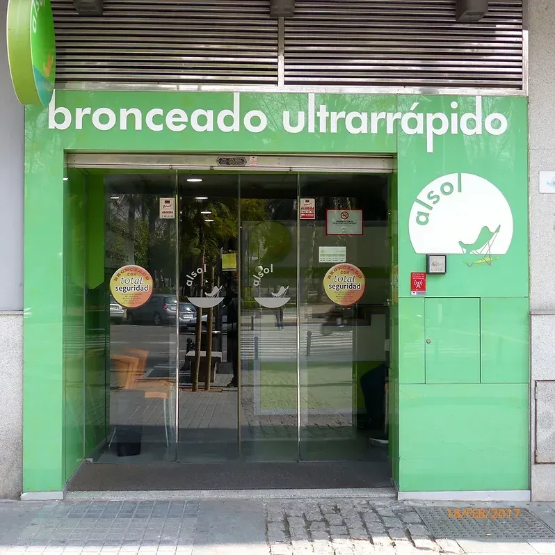 Entrada verde a un salón de bronceado con puertas corredizas de vidrio. Se ve el texto