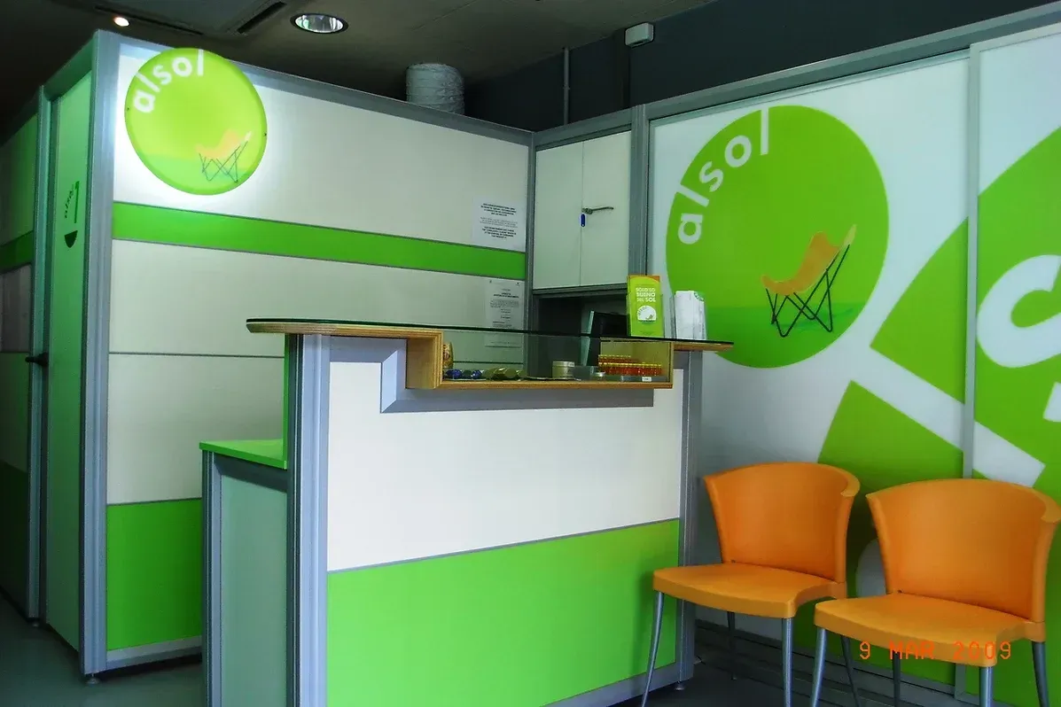 Área de recepción con paredes verdes y blancas, sillas naranjas y el logo