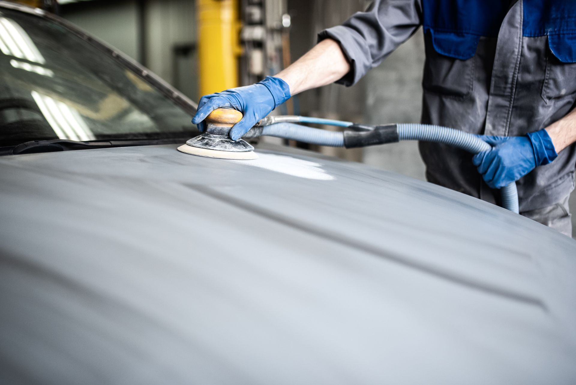 Ein Mann schleift in einer Garage die Motorhaube eines Autos.