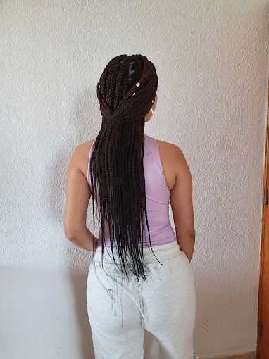 Una mujer con trenzas largas lleva una camiseta morada y pantalones blancos.