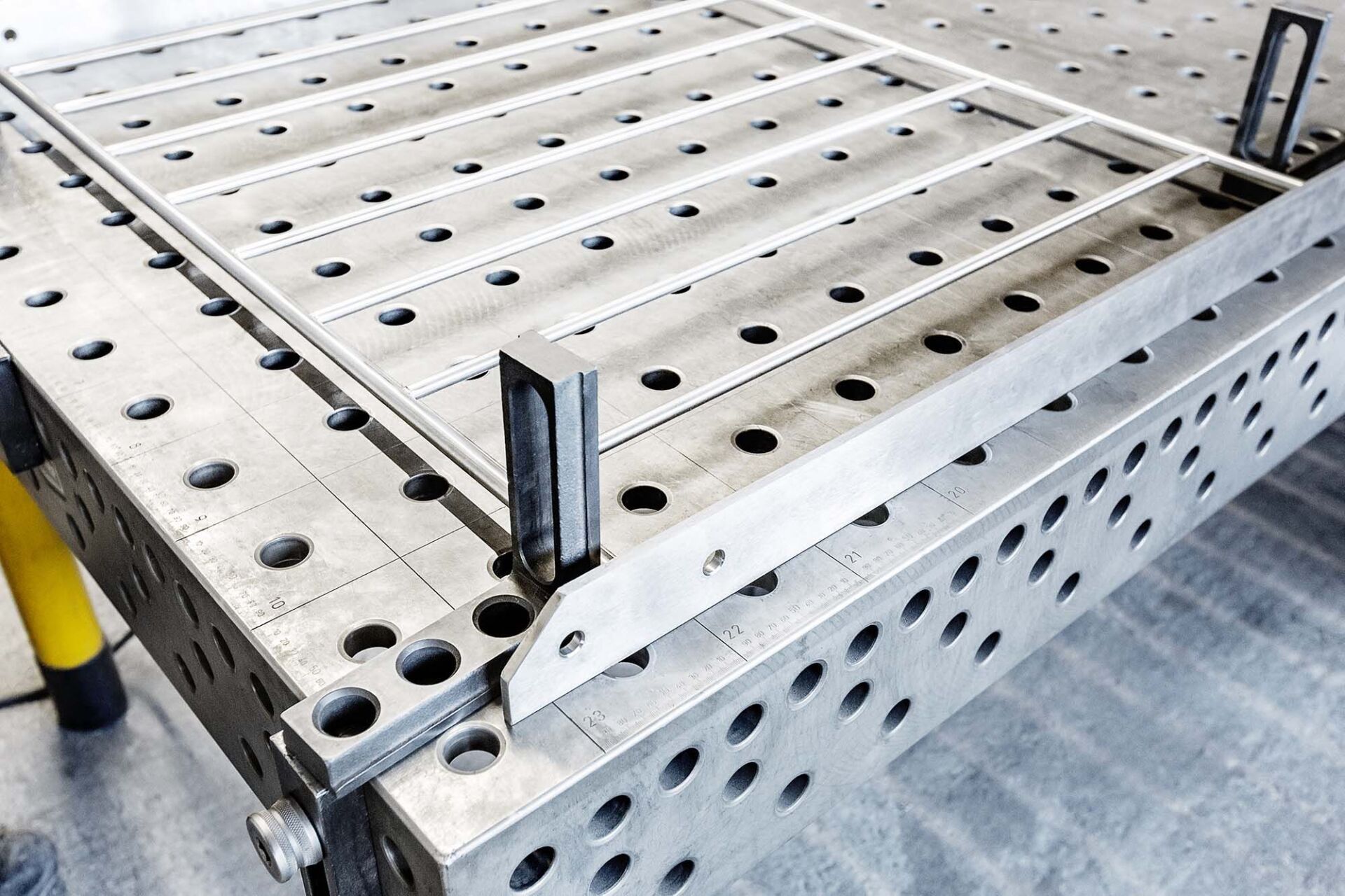Ein Metallrahmen wird auf einem gitterartigen Schweißtisch verschweißt. Klemmen halten die Teile an ihrem Platz.