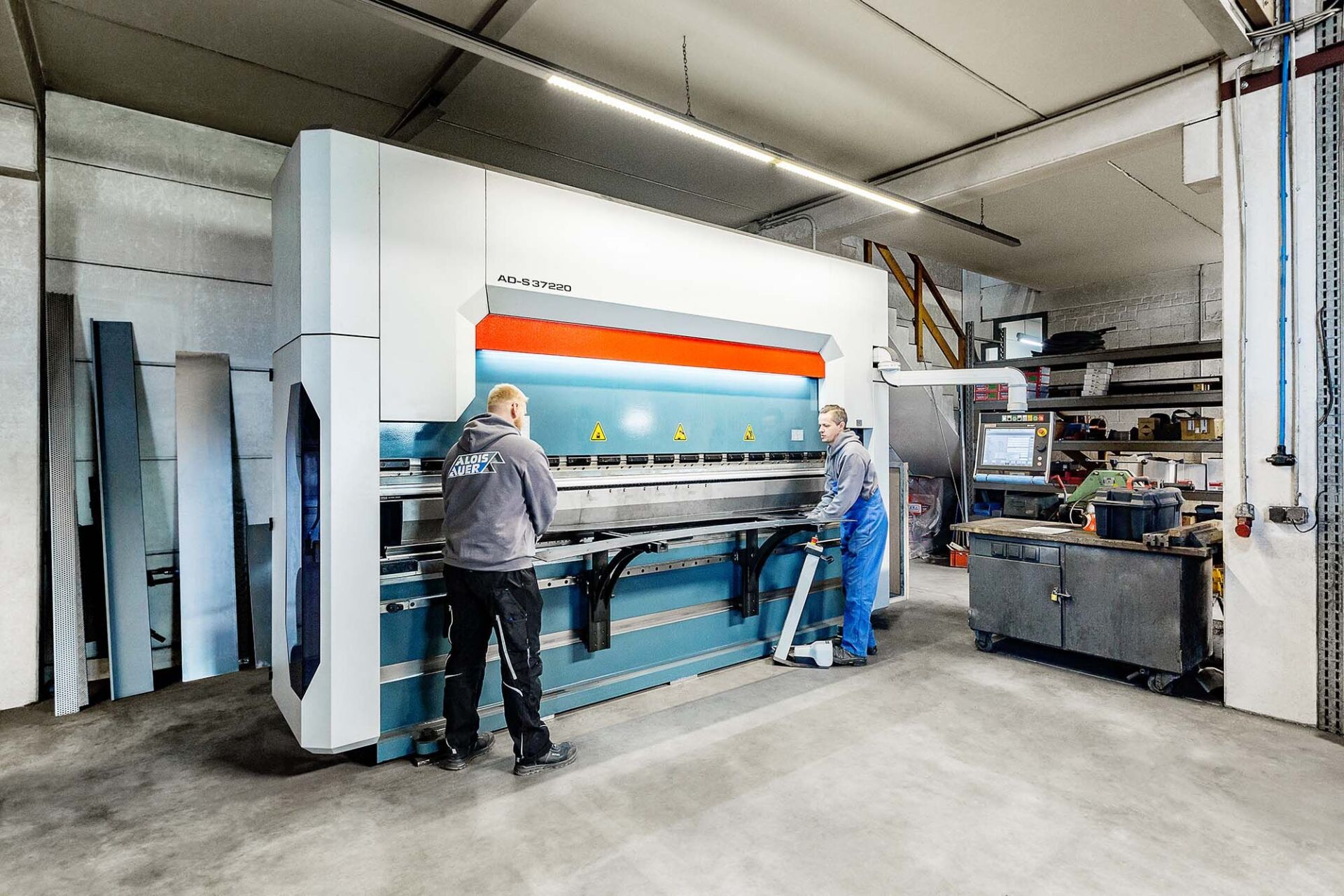 Zwei Arbeiter bedienen in einer Werkstatt eine große Metallbiegemaschine.