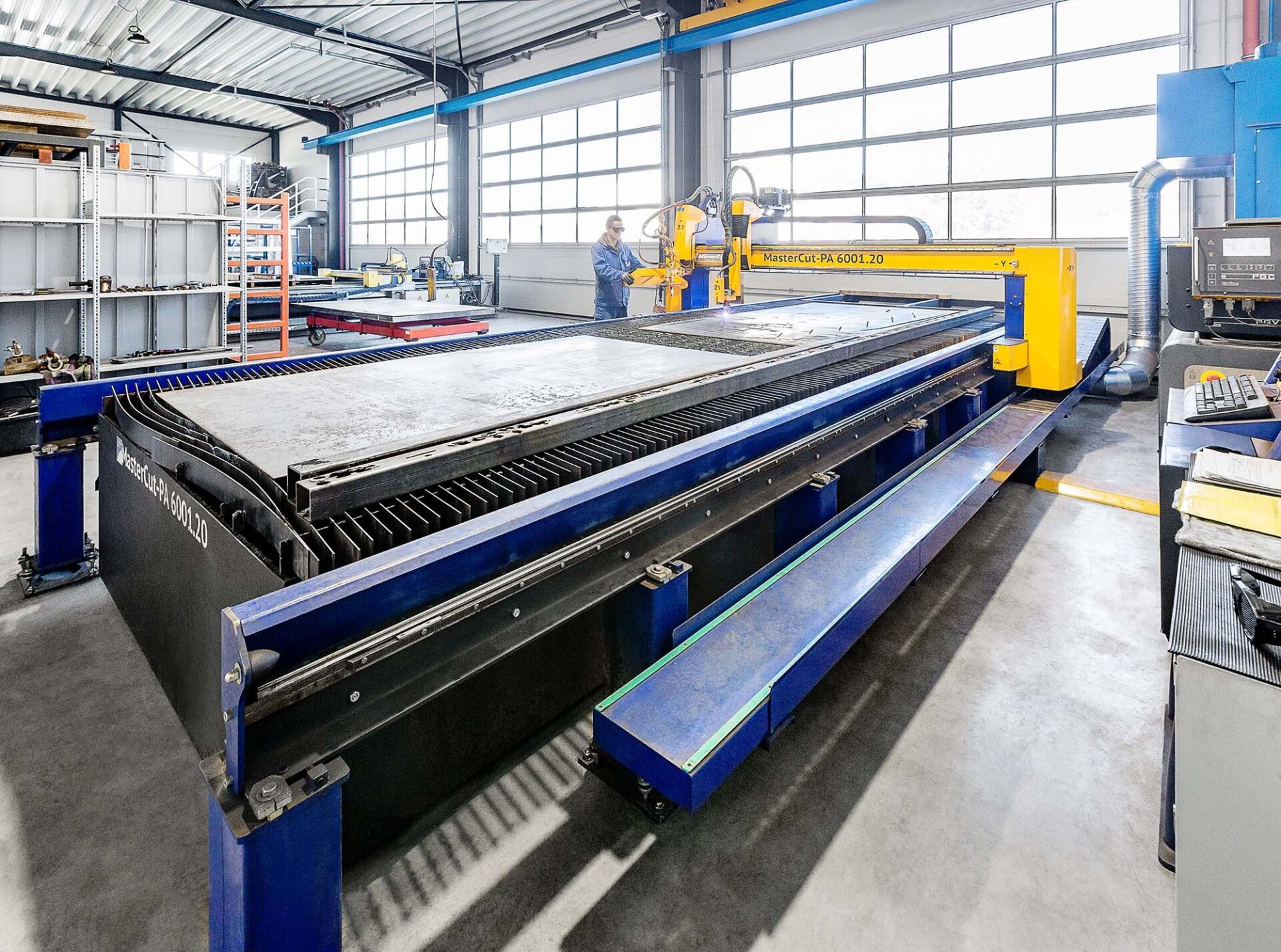 Eine große industrielle CNC-Schneidemaschine in einer Fabrik. Ein Arbeiter befindet sich in der Nähe der Maschine.