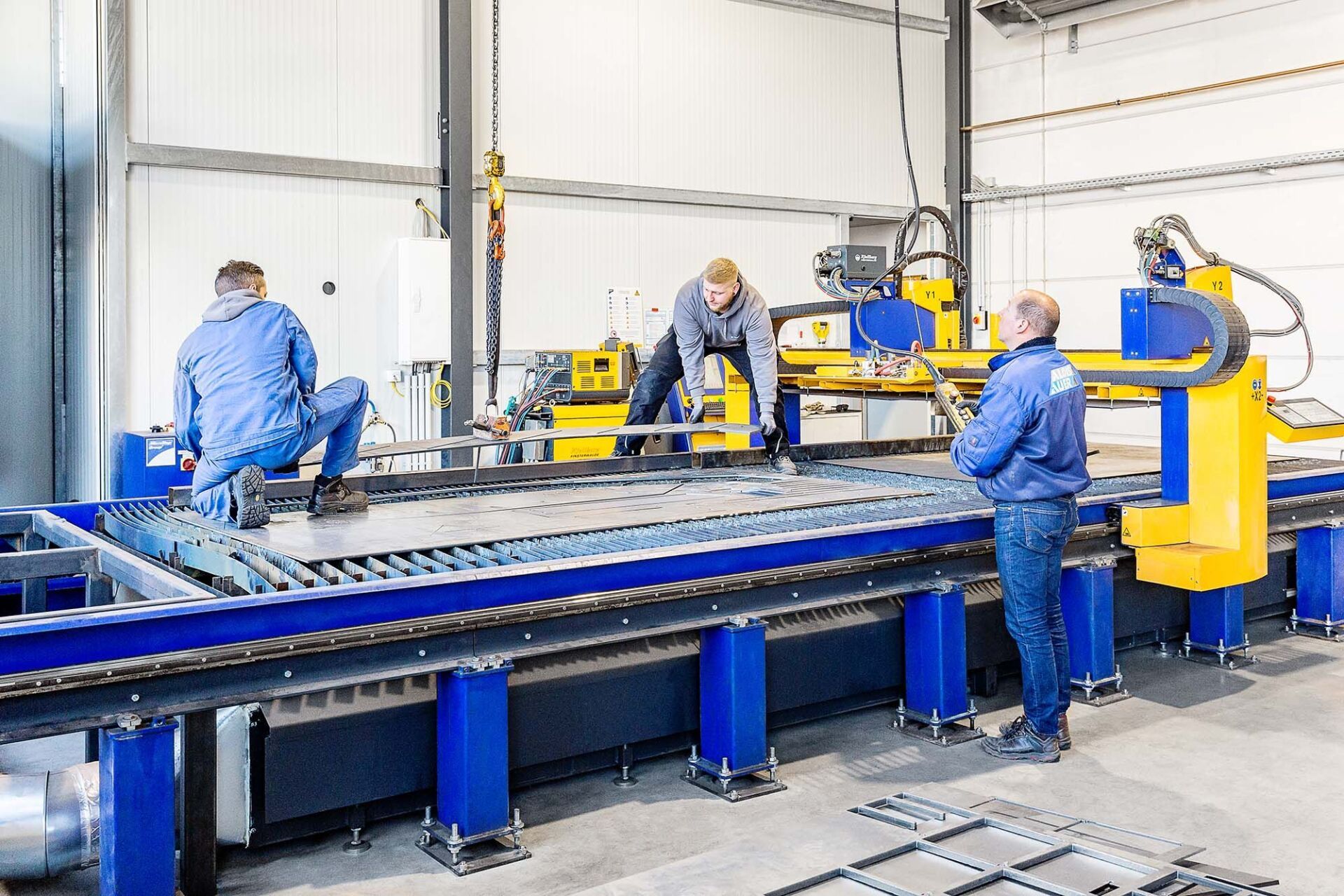 Drei Arbeiter bedienen eine Metallschneidemaschine in einer Fabrik.