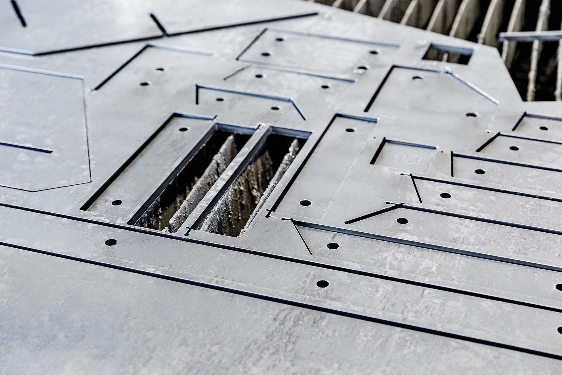 Graue Metallplatten mit verschiedenen Ausschnittformen und Löchern.
