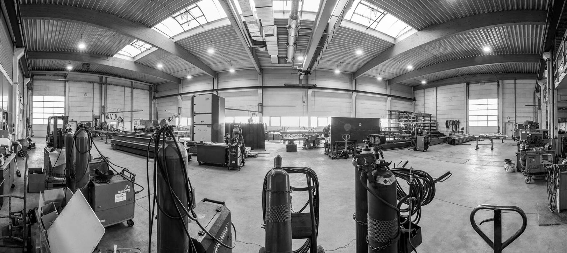 Eine Graustufenaufnahme des Innenraums einer großen Industriewerkstatt; zu sehen sind Ausrüstung, Werkzeuge und Werkbänke.