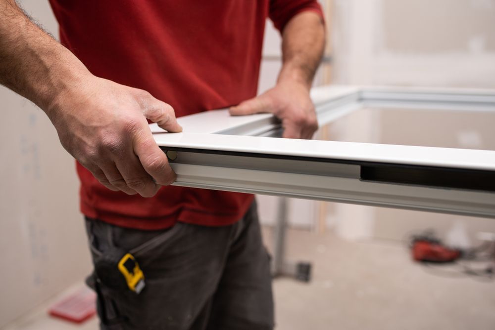 Hombre con camisa roja sosteniendo un marco de ventana blanco durante la instalación en interiores.