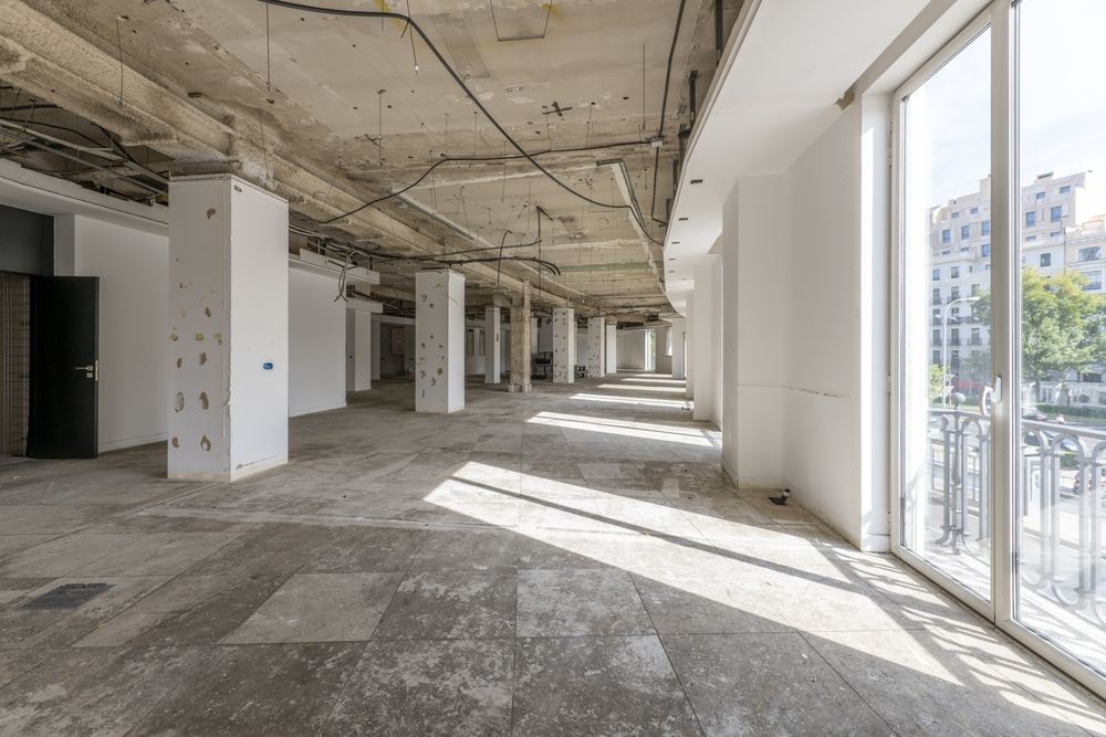 Local comercial vacío en proceso de remodelación; columnas de hormigón, cableado expuesto, grandes ventanales con vista a la ciudad.