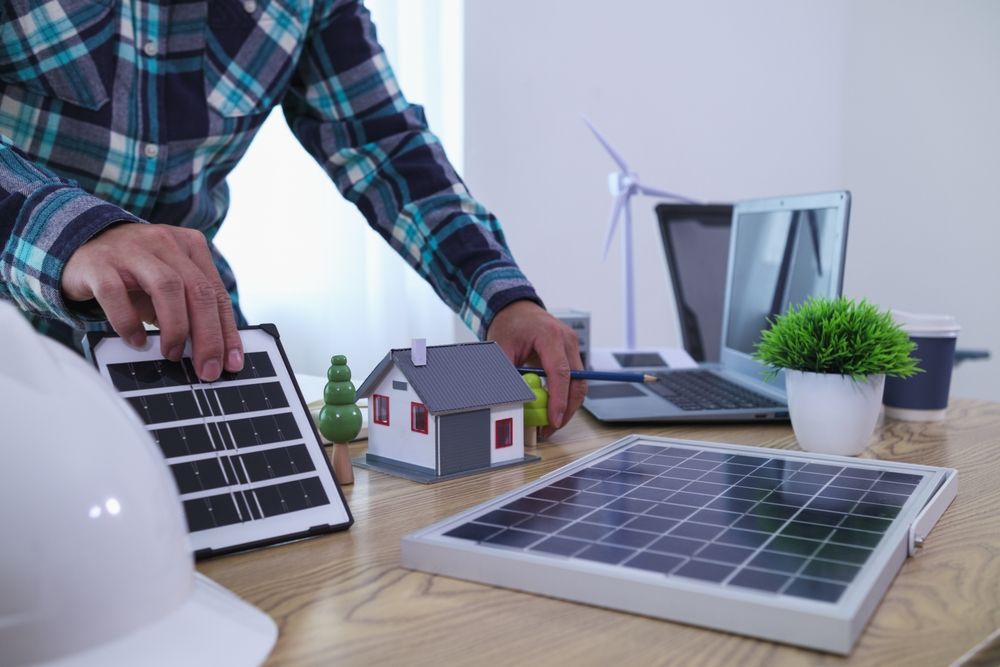 Persona con paneles solares y modelo de casa en el escritorio, concepto de energía renovable.