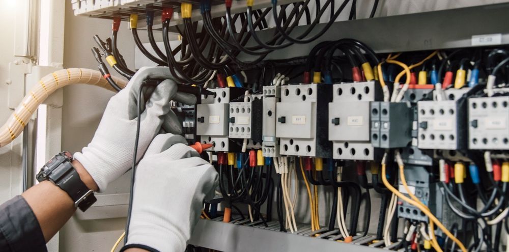 Electricista con guantes probando cables en un panel eléctrico.