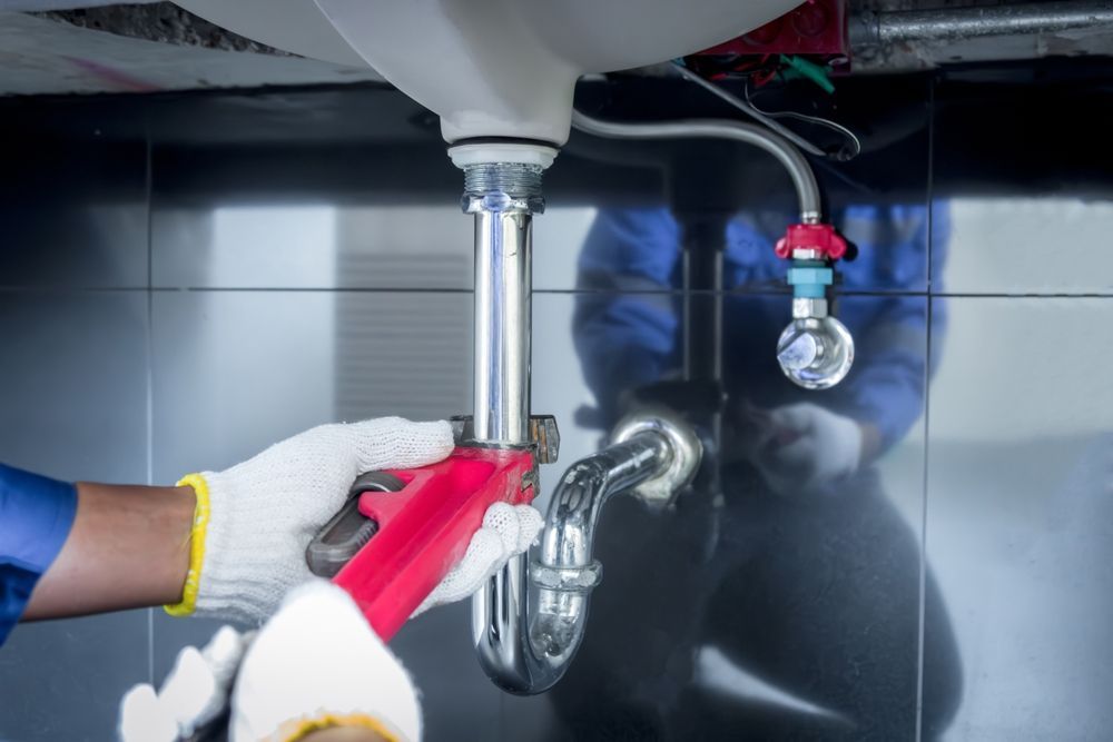Fontanero con uniforme azul trabajando debajo de un fregadero, usando una llave inglesa en una tubería.