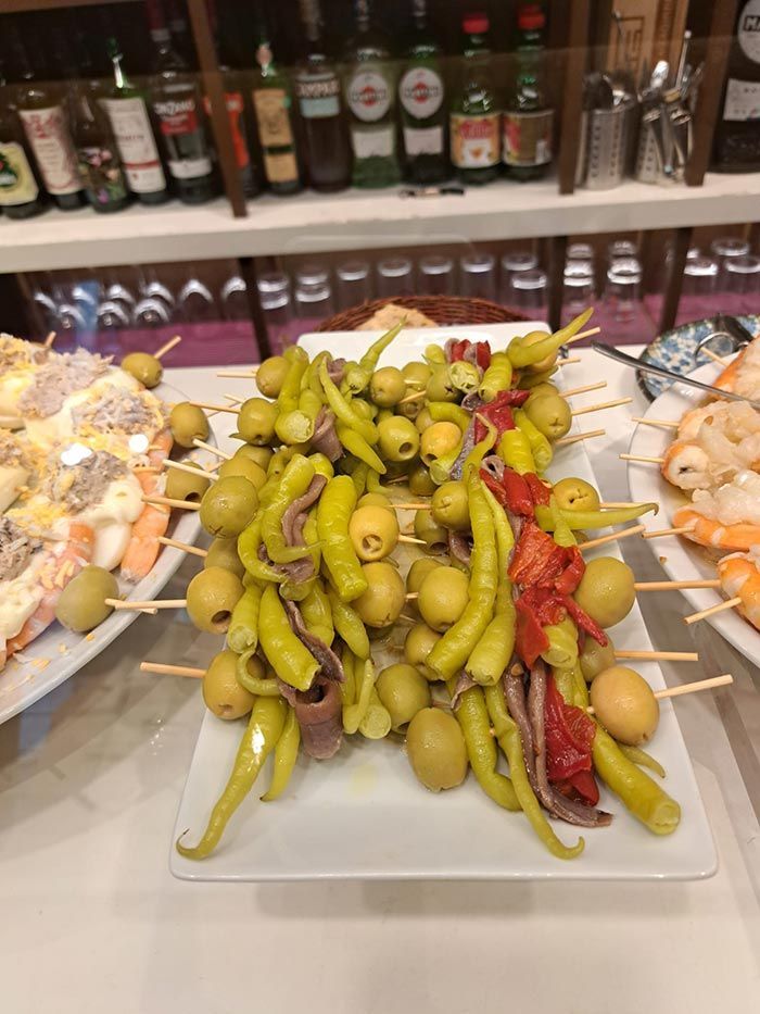 Un plato blanco cubierto con pimientos verdes y aceitunas en brochetas.