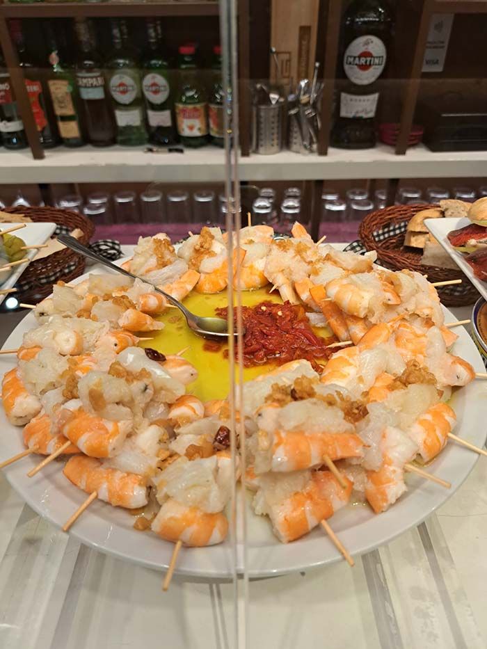 Un plato de camarones en brochetas con una cuchara sobre una mesa.